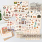 A collage of multiple sticker sheets featuring hand-drawn autumn and cozy illustration motifs, with text reading 'Bonus Sticker Pack (396 stickers)' and 'Each illustration and icon is carefully hand-drawn by me.' The sheets include seasonal and everyday cute drawings such as pumpkins, leaves, books, mugs, and storefront scenes, arranged on a light surface with a small plant and cup nearby.